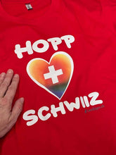 Carica l&#39;immagine nel visualizzatore di Gallery, T-Shirt in Rot, mit Hopp Schwiiz und einem farbigen  (Regenbogen) Herz mit Schweizerkreuz
